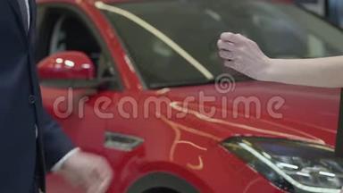 未识别的推销员给未识别的女商人一把汽车钥匙，并在汽车经销商中握手。 汽车陈列室